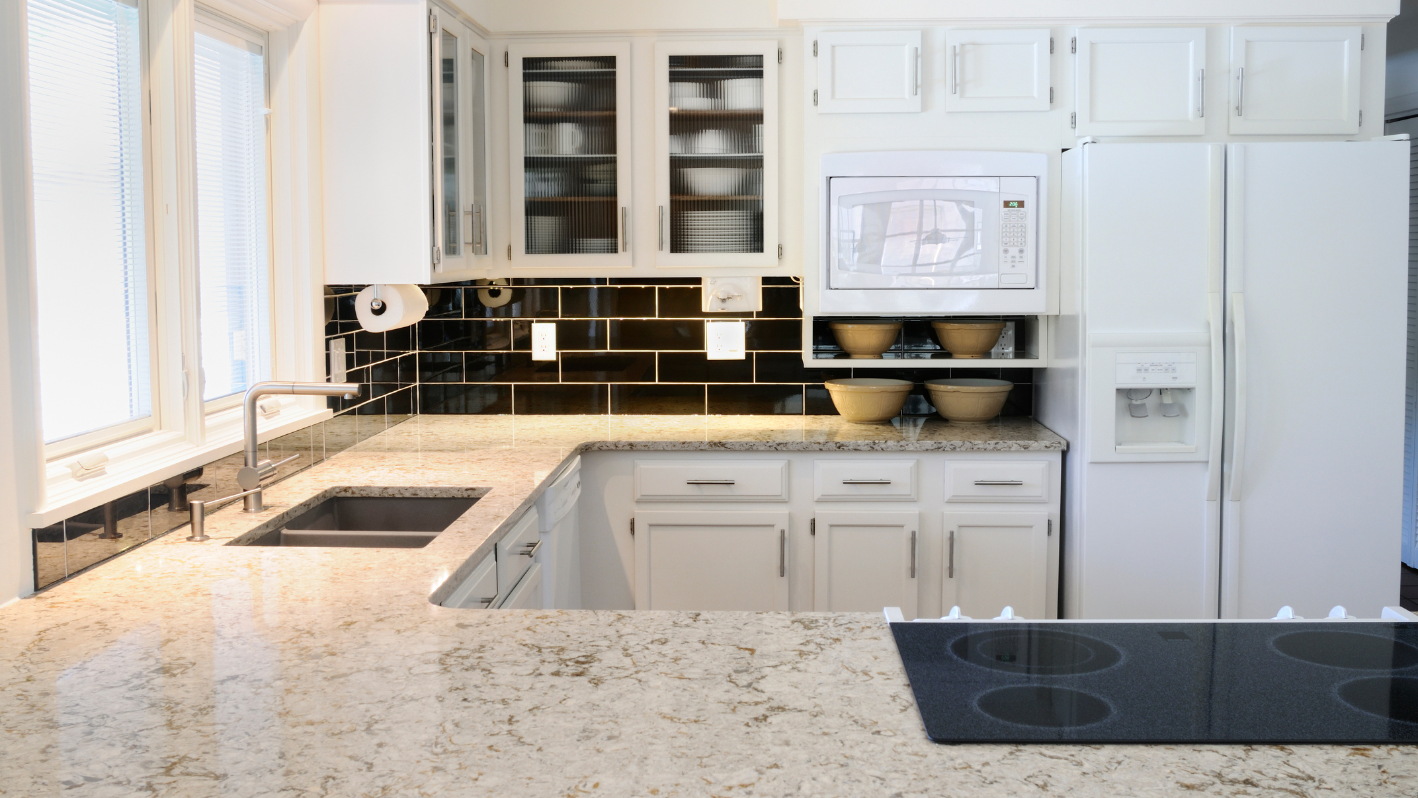 A kitchen with white cabinets and marble counter tops