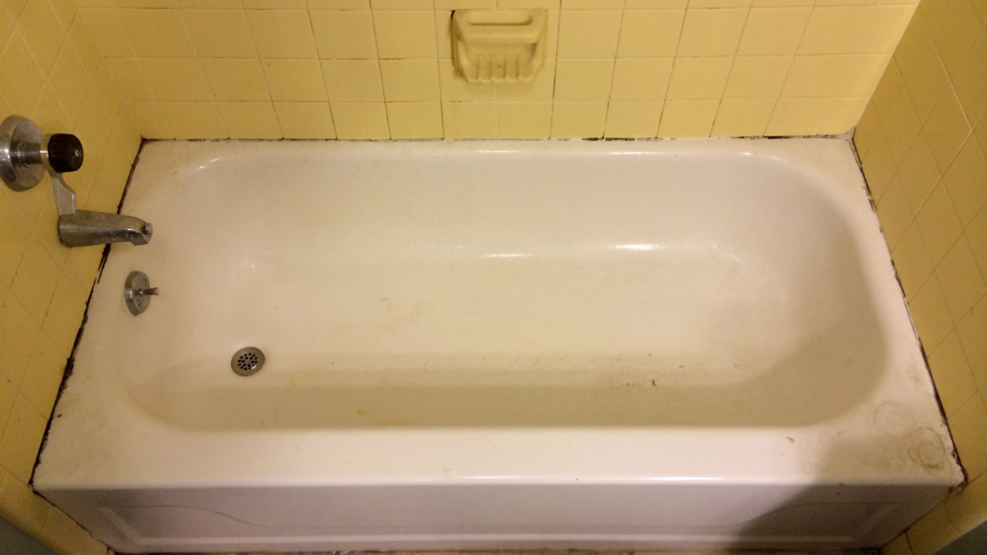 A dirty bathtub in a yellow tiled bathroom